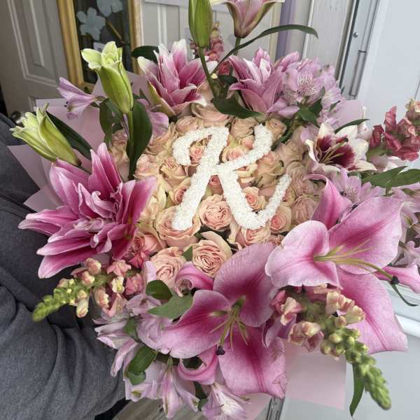 Pink lilies and roses arranged around a white floral letter R.