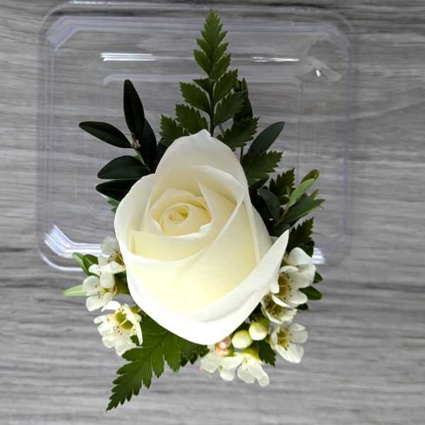 White rose boutonniere with small white blossoms and greenery