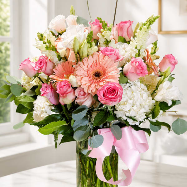 Pink and white mixed bouquet in a glass vase with a pink ribbon