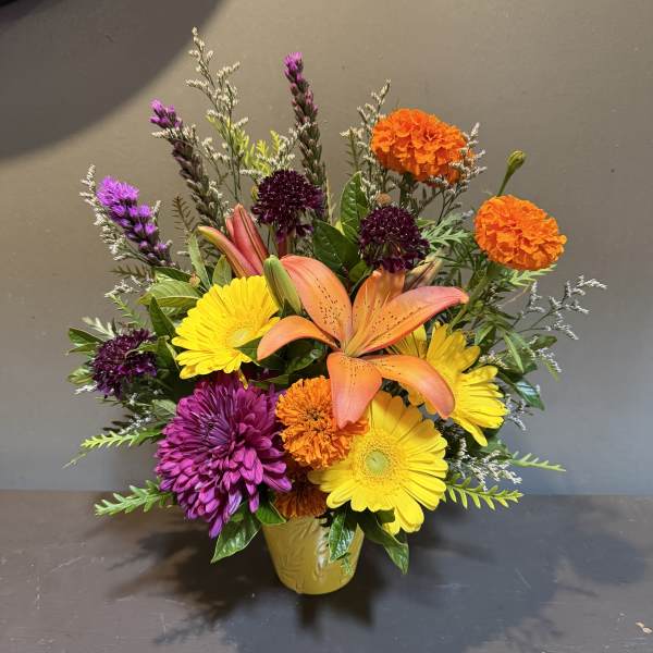 Colorful mixed flower arrangement in a yellow vase with lilies and daisies