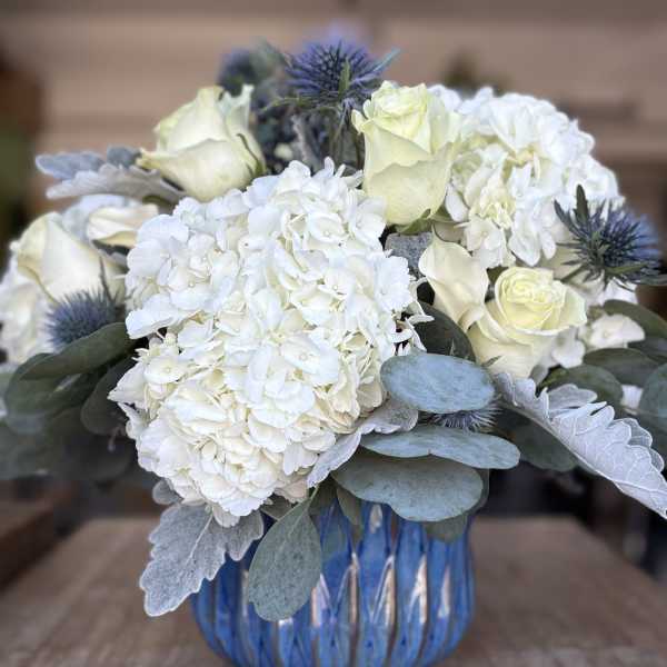 White hydrangeas and pale roses in a blue glass vase