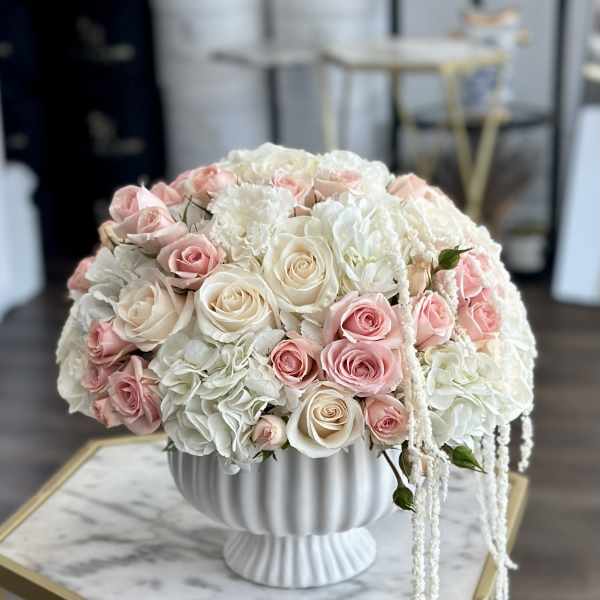 Round bouquet of blush and white roses in a white pedestal vase