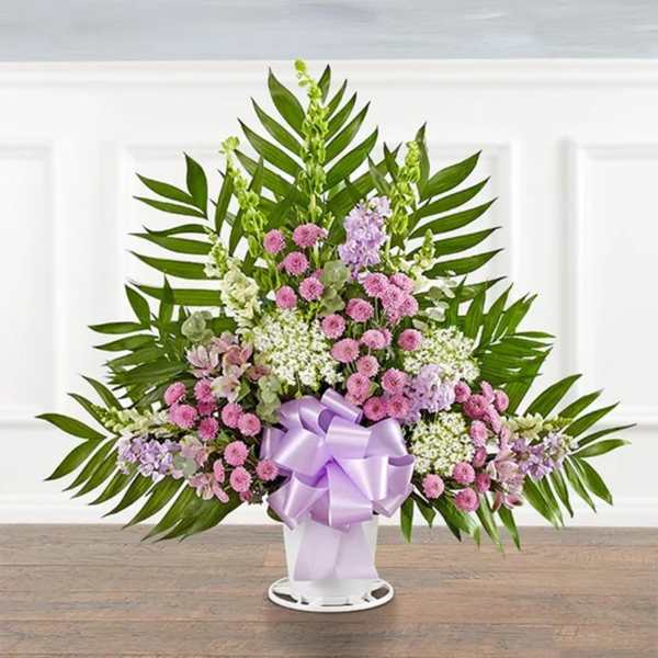 Standing floral spray with pink and lavender blooms in a white vase with a purple bow