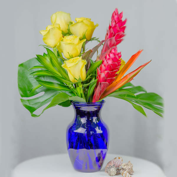 Yellow roses and tropical flowers in a blue glass vase