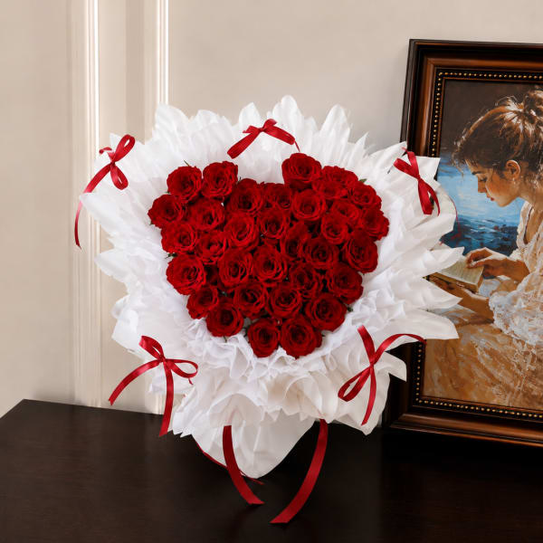 Heart-shaped bouquet of red roses with white wrapping and red ribbons