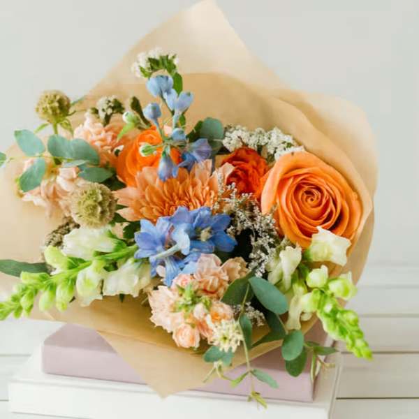 Bouquet of orange, blue, and peach flowers wrapped in tan paper