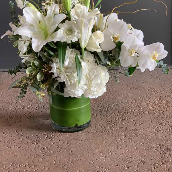 White lilies and orchids arranged in a green vase