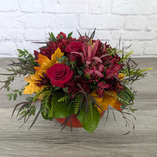 Bouquet of red roses and burgundy flowers in a low orange container