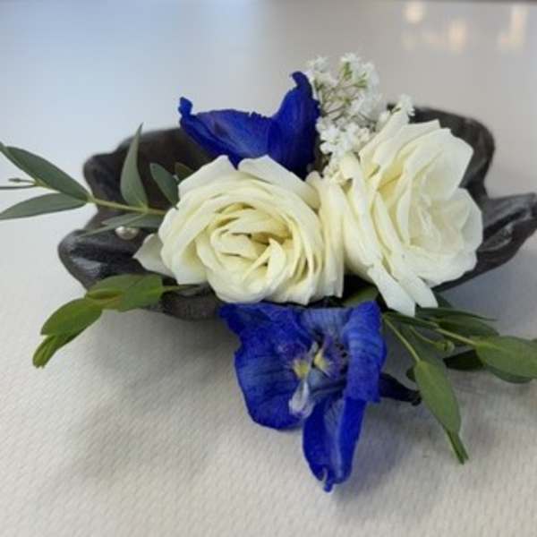 Small floral corsage with white roses and blue flowers on a dark base