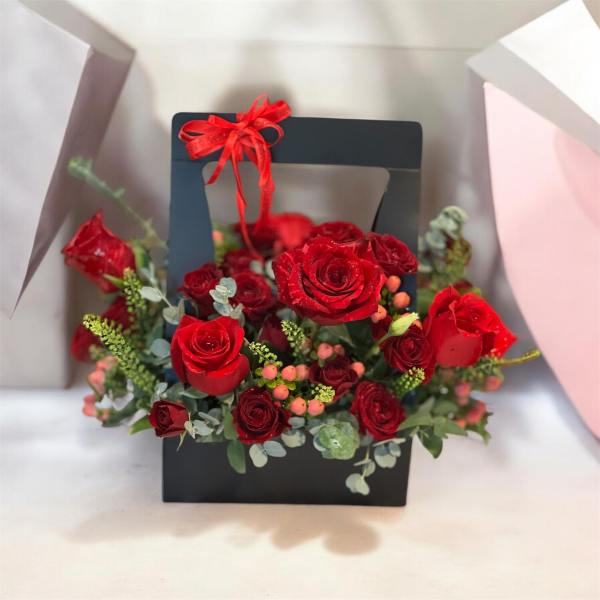 Red roses arranged in a black gift box with a red ribbon