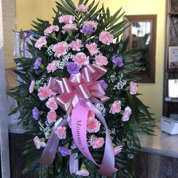 Standing floral spray of pink and purple carnations with a pink ribbon