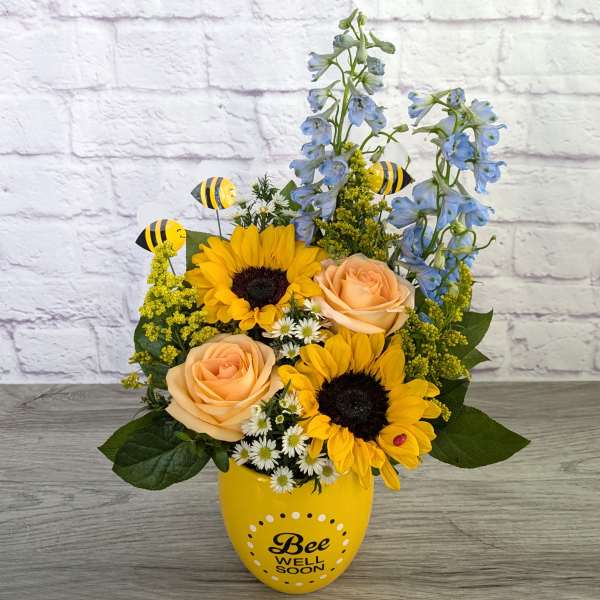 Sunflowers and peach roses in a yellow vase with bee decorations