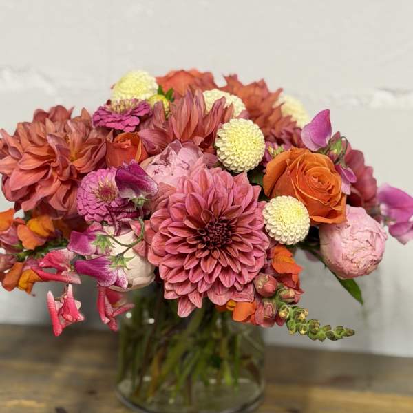 Mixed bouquet of pink, orange, and cream flowers in a glass vase