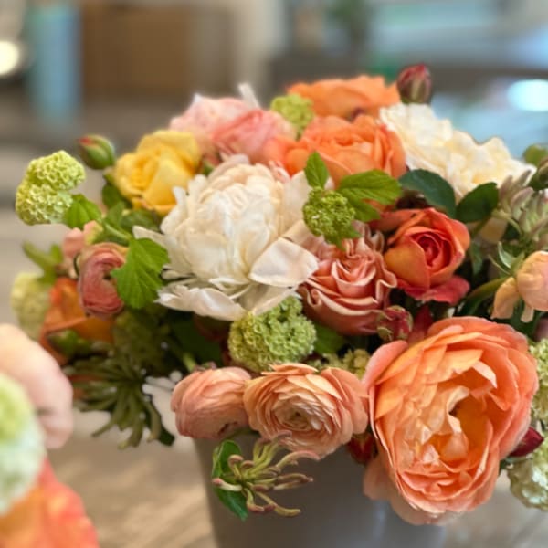 Mixed bouquet of peach, white, and yellow flowers in a gray vase
