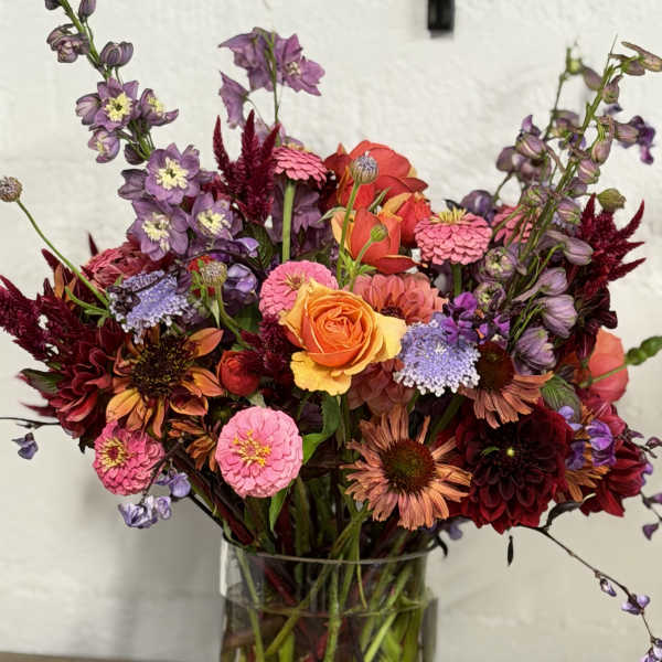 Mixed bouquet of orange, pink, purple, and burgundy flowers in a glass vase