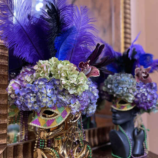 Decorative mask topped with purple hydrangeas and feathers