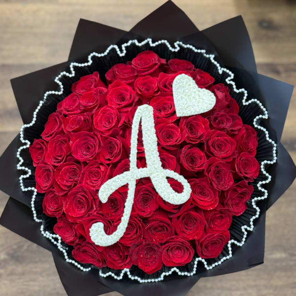 Round arrangement of red roses with a white A initial and heart on top, wrapped in black paper