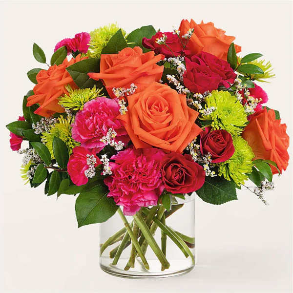 Mixed bouquet of orange, pink, and red flowers in a clear glass vase