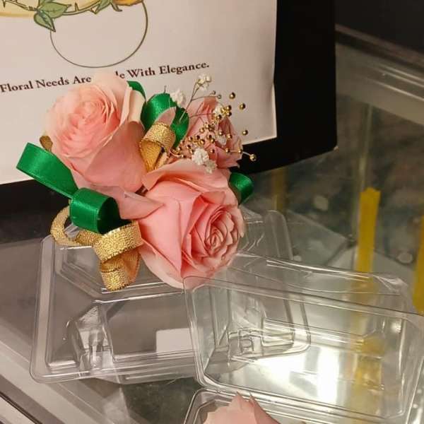 Pink rose boutonnieres in clear plastic boxes with green and gold ribbon