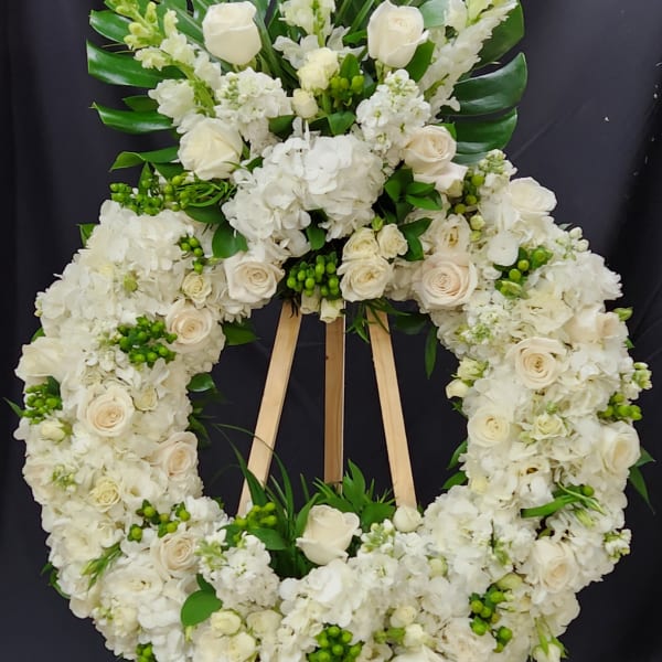 White floral funeral wreath on a wooden easel with roses and hydrangeas