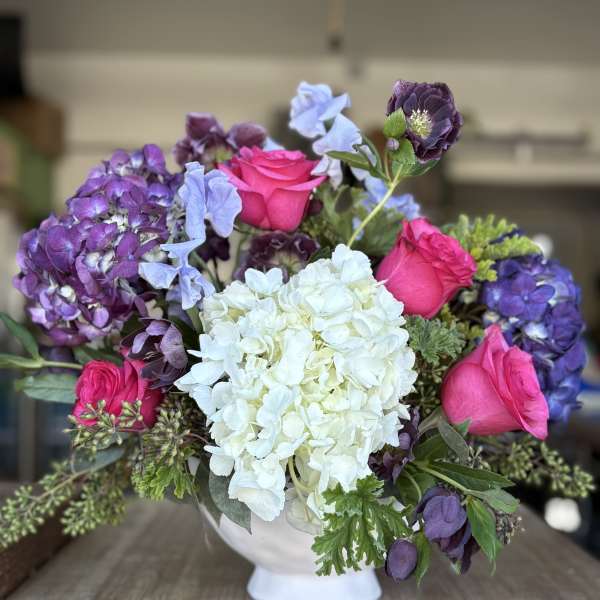 Bouquet of pink roses, white hydrangea, and purple blooms in a white vase