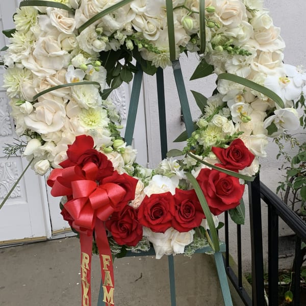 Large floral wreath of white and red roses on an easel with a red bow