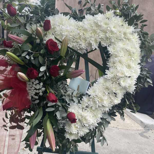 Heart-shaped floral wreath with white chrysanthemums and red roses on an easel