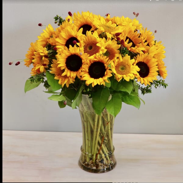 Tall bouquet of yellow sunflowers in a clear glass vase with visible stems