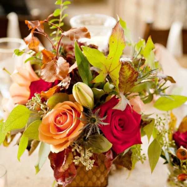 Autumn floral arrangement with red and peach roses in a small vase