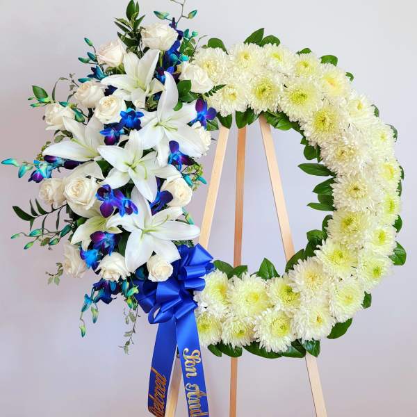 White floral funeral wreath on an easel with blue ribbon