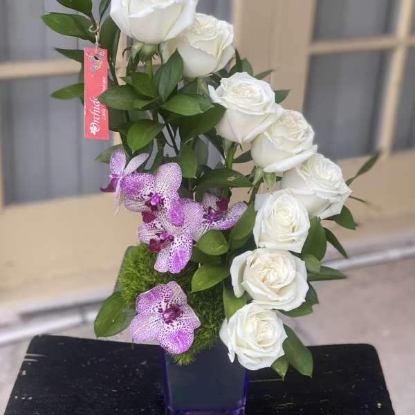 White roses and purple orchids in a square vase