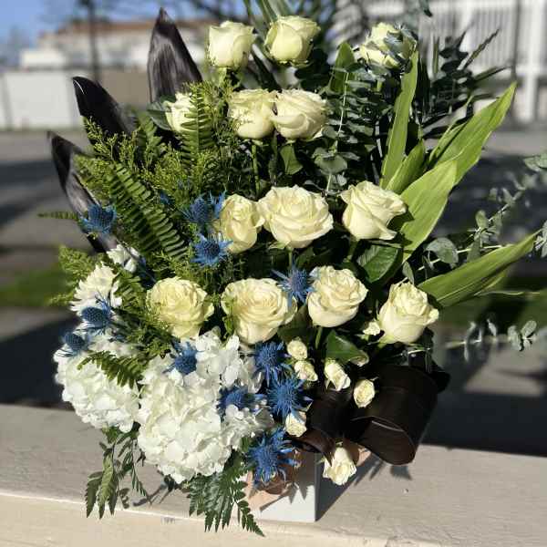 Bouquet of white roses, hydrangeas, and blue thistle in a box