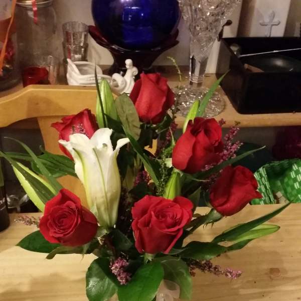 Red roses and a white lily in a clear glass vase with ribbon.