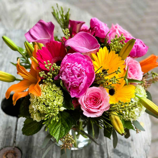 Mixed bouquet with pink, yellow, and orange flowers in a glass vase