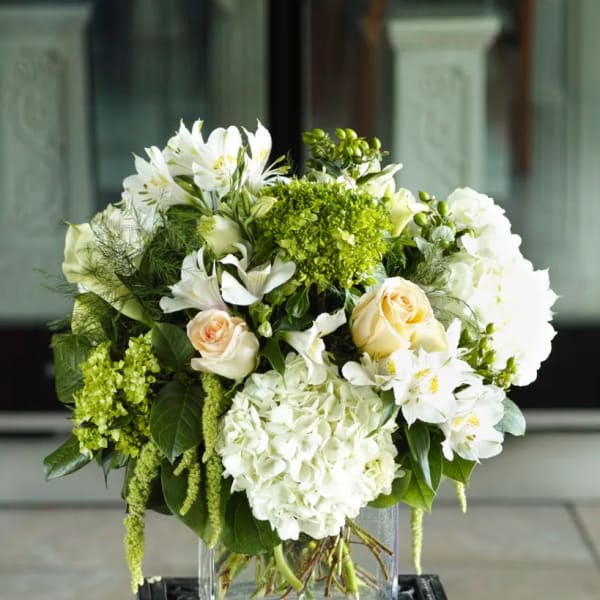White and green floral arrangement in a clear square vase