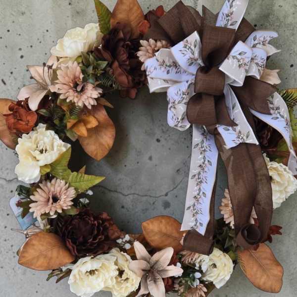 Floral wreath with cream blooms, brown flowers, and a large ribbon bow
