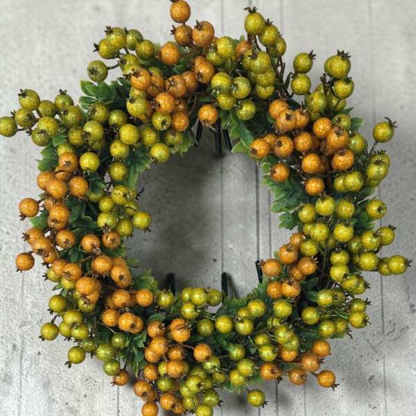Round wreath of orange and green berries on a gray background