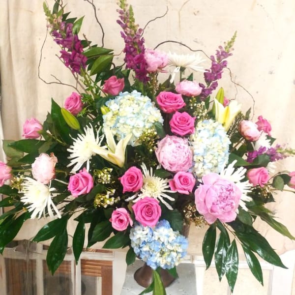 Large mixed floral arrangement with pink roses, blue hydrangeas, and white lilies in a vase.