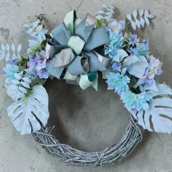 Pastel floral wreath with a large ribbon bow and white monstera leaves