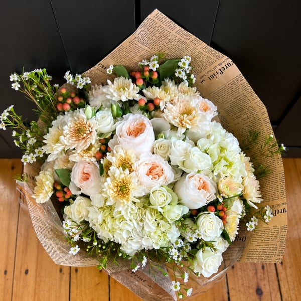 Bouquet of white and peach flowers wrapped in newspaper-style paper