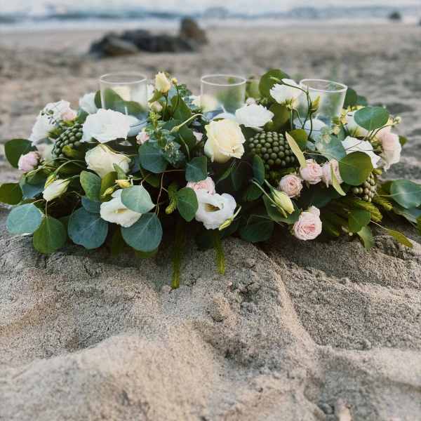 Low floral centerpiece with white and blush blooms on a beach