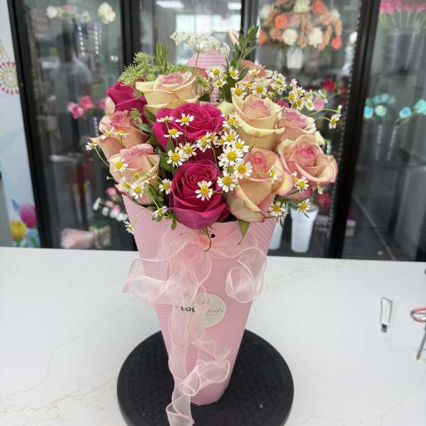 Pink and cream roses with small white daisies in a pink cone wrap