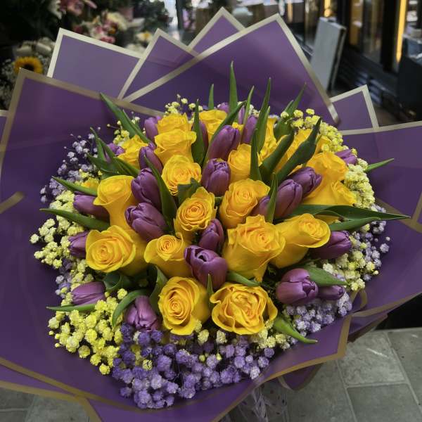 Bouquet of yellow roses and purple tulips wrapped in purple paper