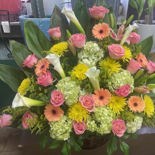 Large mixed bouquet with pink roses, white calla lilies, and yellow flowers in a basket