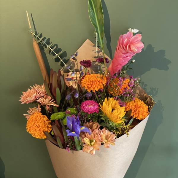 Hand-tied bouquet of mixed pink, orange, yellow, and purple flowers in kraft paper