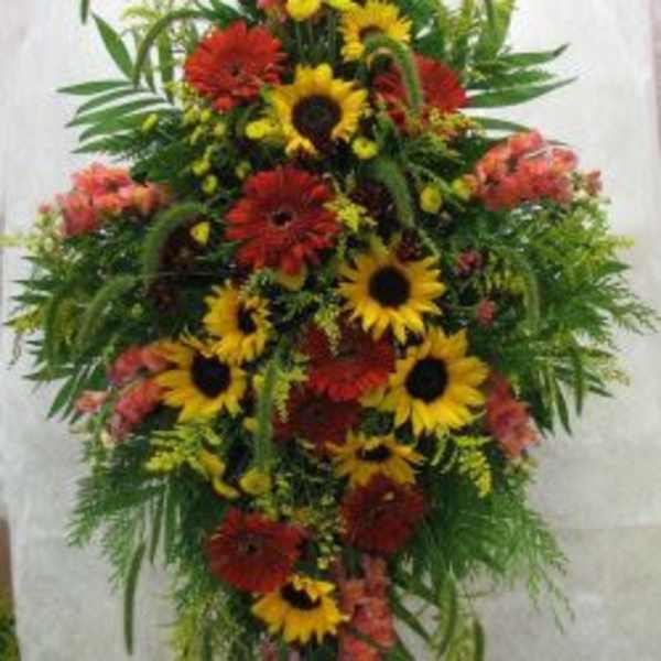 Tall standing spray of sunflowers and red daisies with greenery
