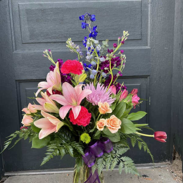 Mixed bouquet of pink lilies, roses, and purple flowers in a glass vase