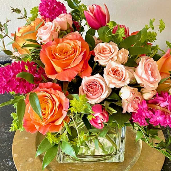 Mixed bouquet of orange and blush roses with pink blooms in a glass vase.