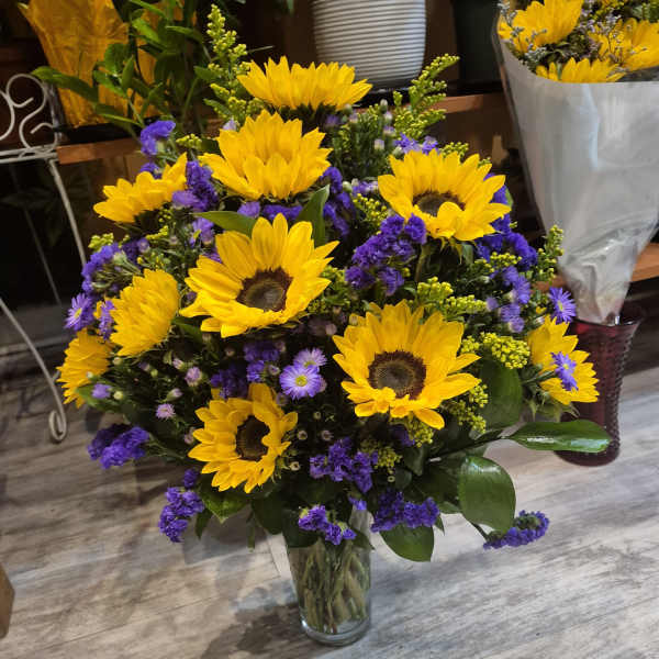 Bouquet of yellow sunflowers and purple filler flowers in a clear glass vase.