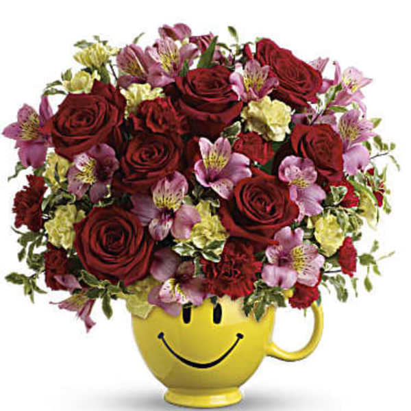Bouquet of red roses and pink flowers in a yellow smiley-face mug